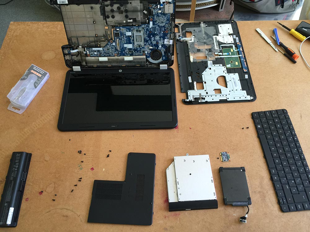 An HP laptop half disassembled. Along the bottom of the screen you can see the battery, bottom case cover, DVD drive, hard drive, keyboard.