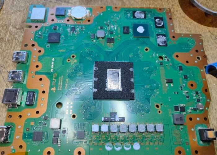 A view of the whole top side of a PlayStation 5 motherboard, as seen during a service at our Sheffield workshop. The chip in the middle is the APU, which generates most of the heat. It gets incredibly hot, so liquid metal is used to carry that heat across to the heatsink.